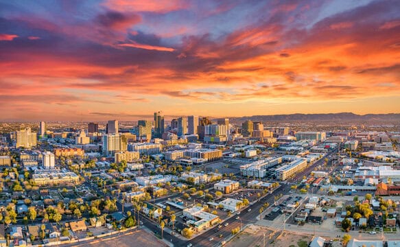 Aerial view of a cityscape at sunset, with a vibrant orange and pink sky. Among the towering skyscrapers in Contra Costa County, known for its managed IT services, mountains loom distantly. Streets and urban greenery spread below, embodying a blend of innovation and natural beauty.