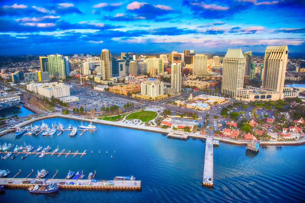 Aerial view of a coastal cityscape in Contra Costa County with numerous skyscrapers and a marina filled with boats. The scene, much like the county's renowned IT support and network security services, is vibrant and dynamic, with partly cloudy skies reflecting on the colorful water.