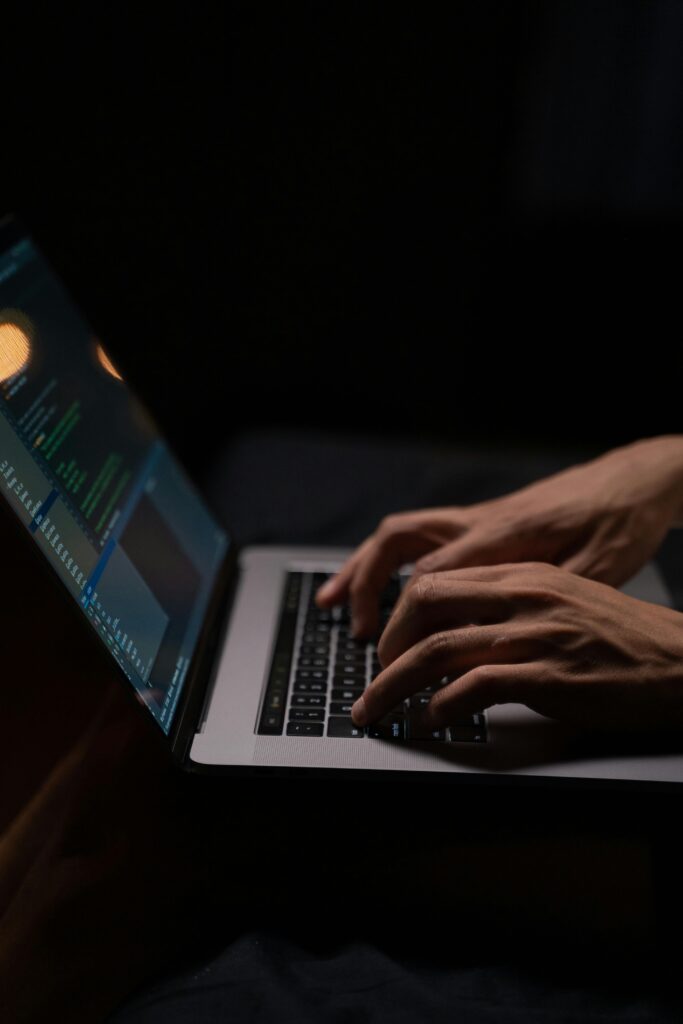 In a dimly lit environment, a person types on a laptop, the screen aglow with lines of code. They're immersed in providing IT solutions for Contra Costa County, ensuring seamless tech support.