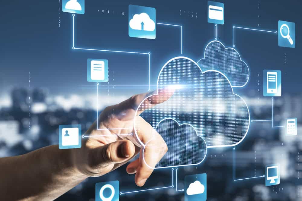 A hand interacts with a digital cloud interface, touching a cloud icon. Surrounded by connected technology symbols and lines, it represents networked data and cybersecurity services in Contra Costa County against a blurred cityscape background.